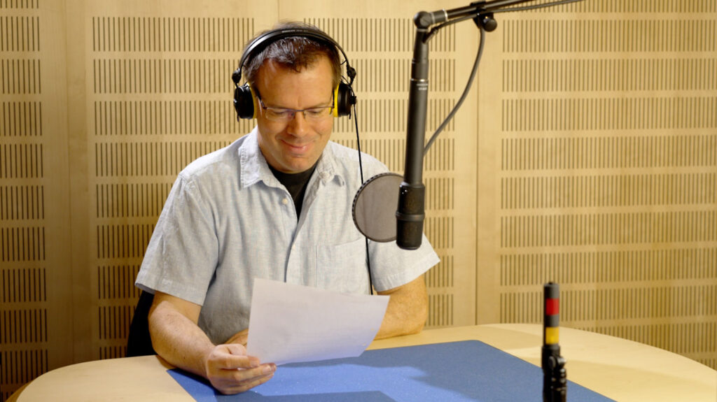 Mann mit Brille, trägt Kopfhörer, spricht in ein Mikrofon im Studio Mann mit Brille, trägt Kopfhörer, spricht in ein Mikrofon im Studio