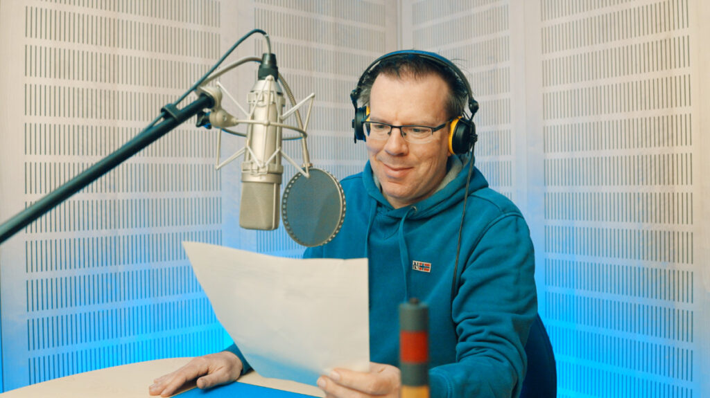 Mann mit Brille, trägt Kopfhörer, spricht in ein Mikrofon im Studio